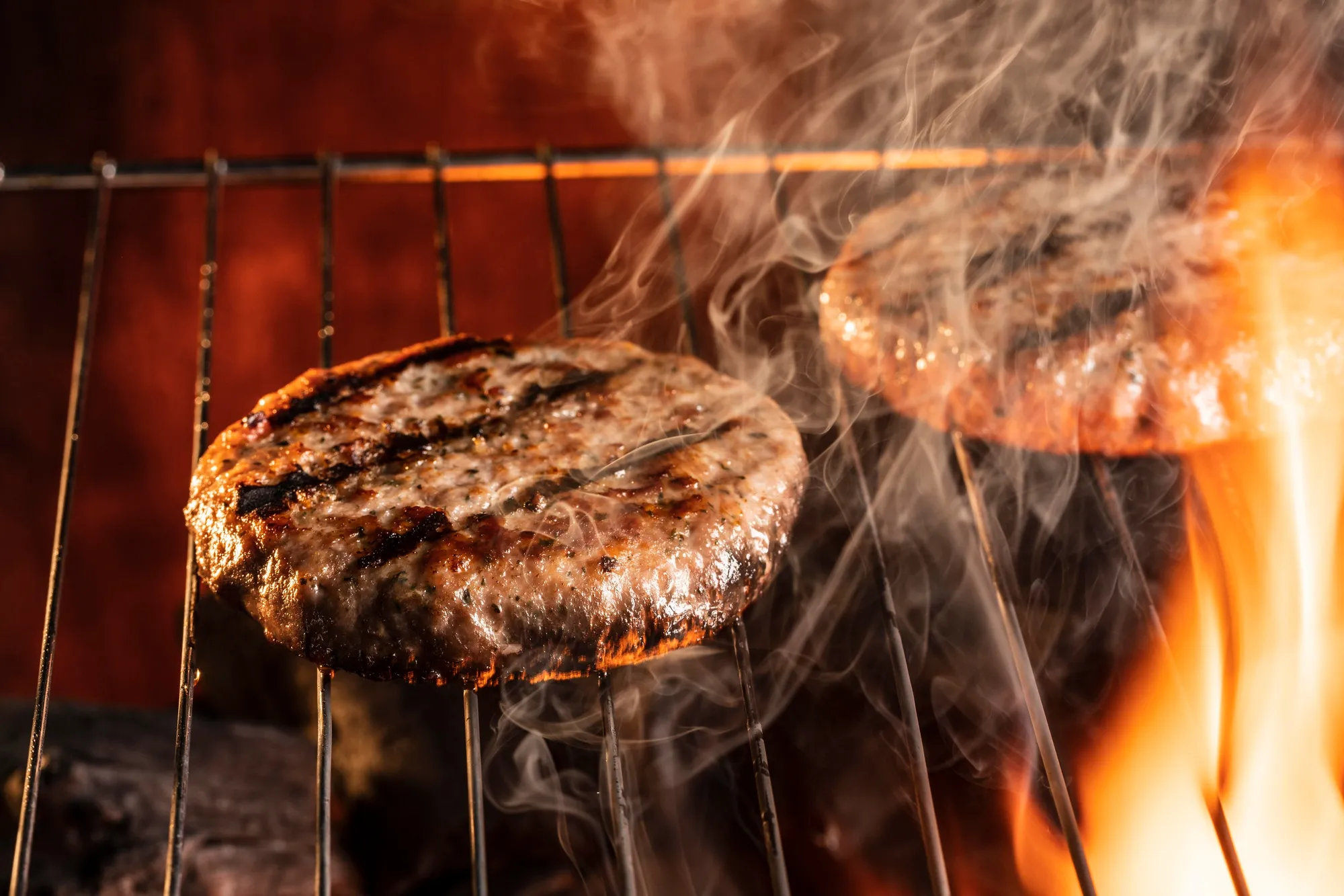 A hamburger cooking on a grill with flames.